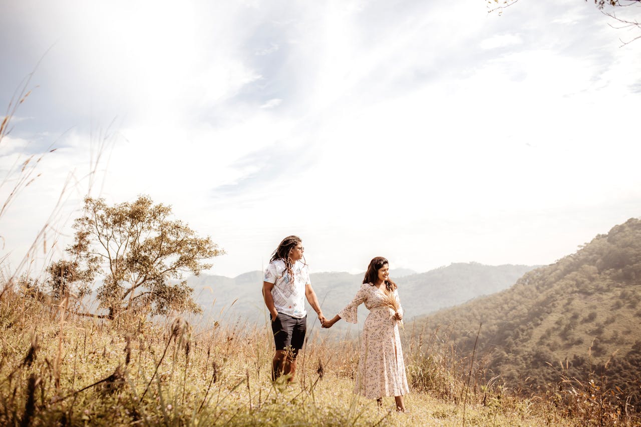 A couple holding hands in a serene meadow with mountains in the background, capturing love and nature.